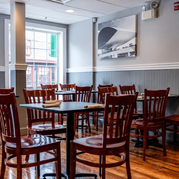 Empty restaurant dining room with dark wooden tables and chairs, and a large window.