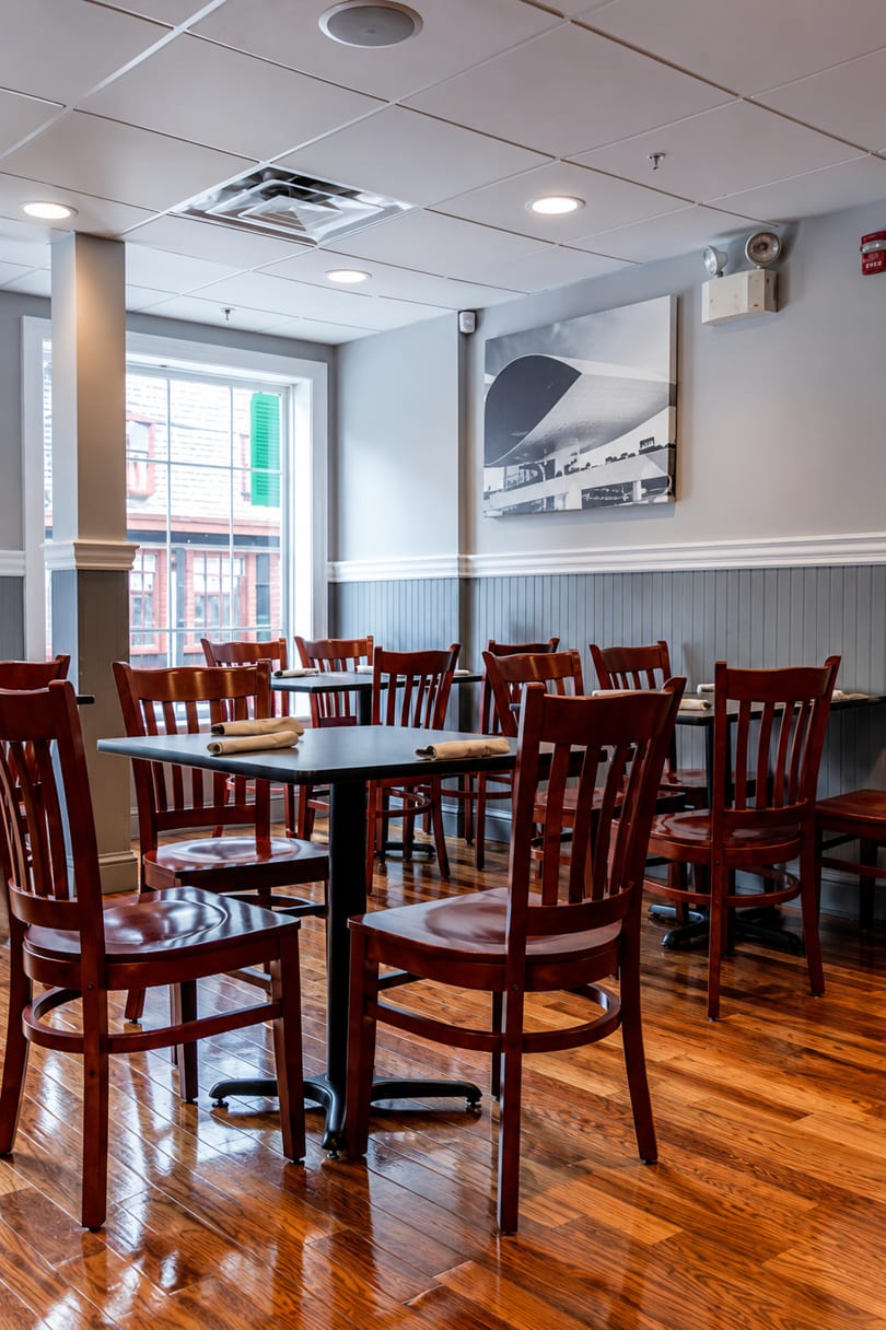 Empty restaurant dining room with dark wooden tables and chairs, and a large window.