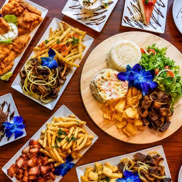 A wooden table laden with various dishes, including fried chicken, fries, pasta, rice, and desserts.