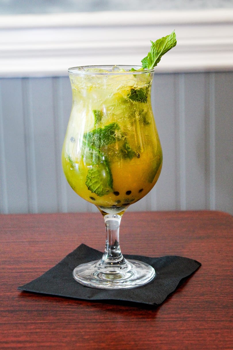 A tall glass of yellow passion fruit mojito with mint leaves and ice on a dark wooden table.
